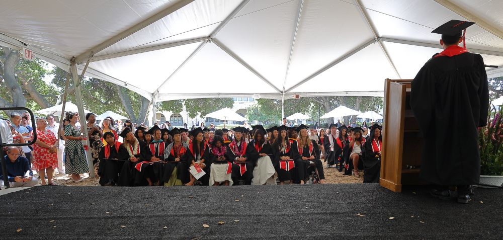 A graduate giving a speech from the stage facing the audience and away from the camera