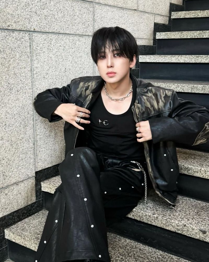 fuma sitting on some broadcasting co’s stairs in all black outfit w black leather jacket. he is holding the jacket open with his hands