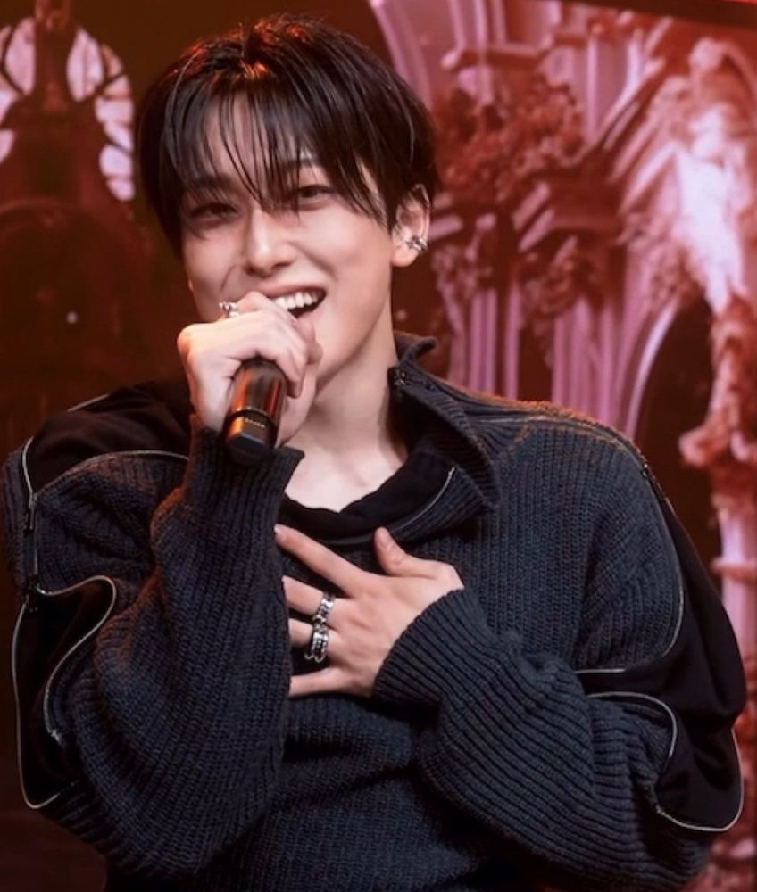 fuma holding mic up to mouth and singing w smile on his face. his other hand is against his chest