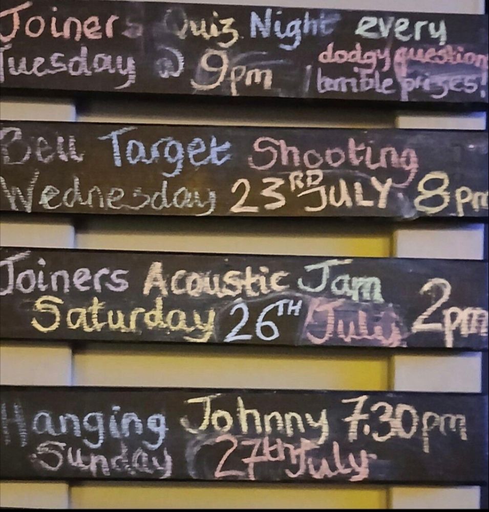 A set of blackboards showing upcoming events at a local pub. First, a quiz, then target shooting, then an acoustic jam session. Finally, on Sunday, they'll be Hanging Johnny
