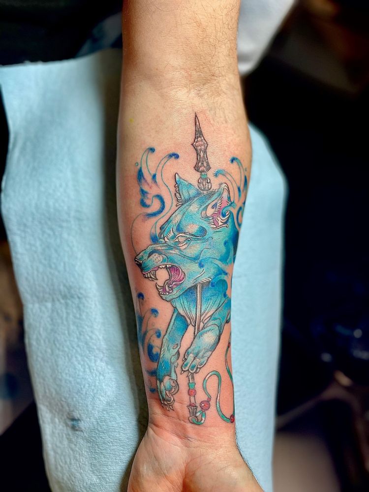 Arm with a blue wolf tattoo with a spear and wave accents.