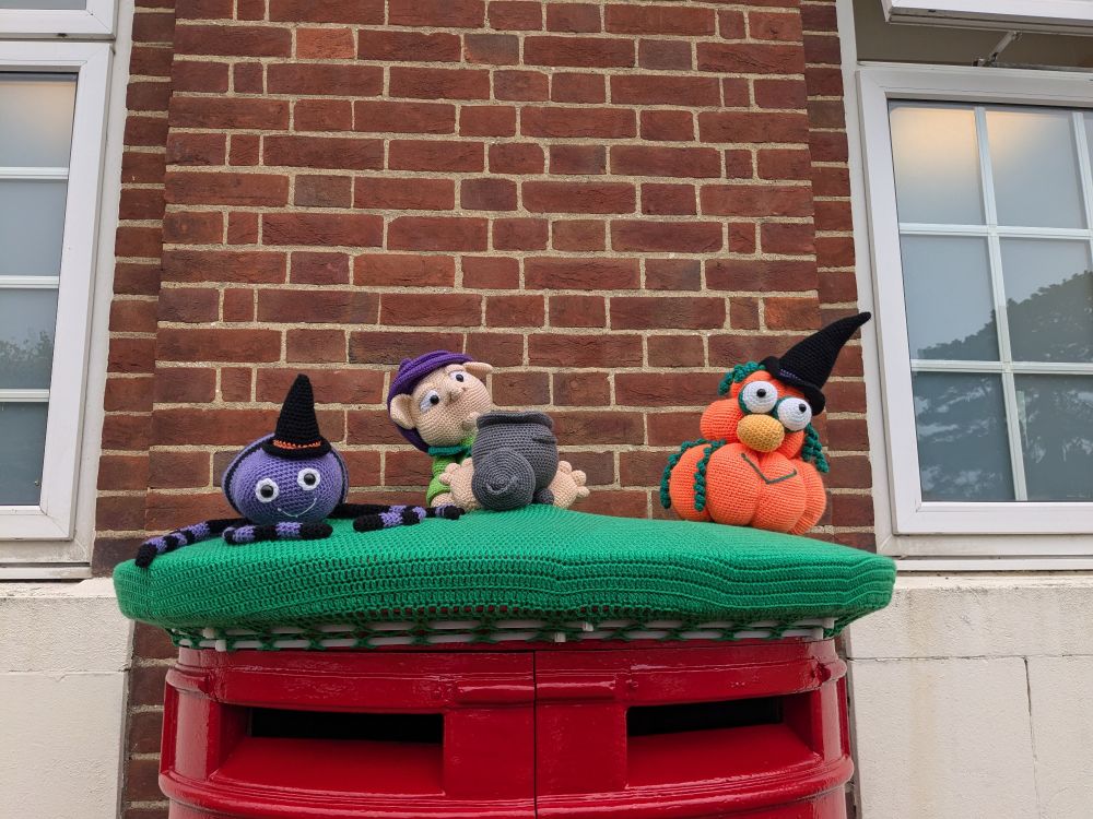 A crochet top on the postbox, with a purple octopus with a witch's hat, an elf near a black cauldron and some pumpkins with googly eyes and witch's hat