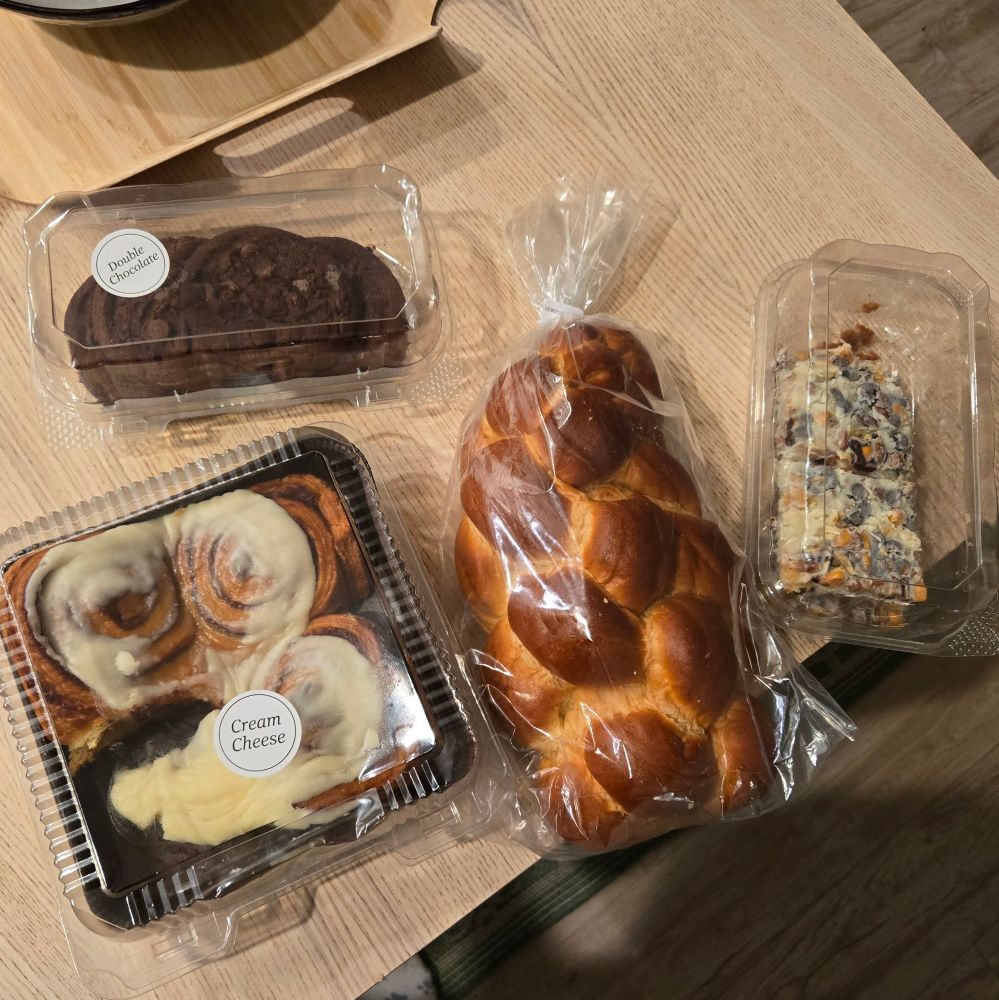 A loaf of challah, some coconut butterscotch bars, chocolate cookies, and a pack of 4 cinnamon rolls with one missing 