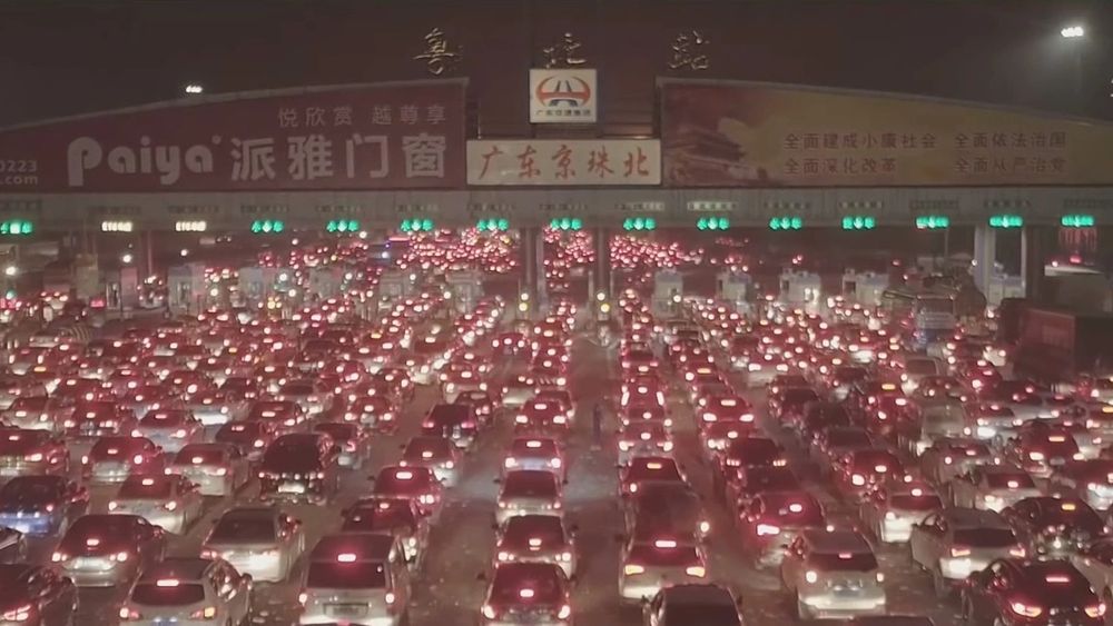 Man sieht eine Autobahn mit 15 Spuren, über alle Spuren erstreckt sich ein großer Stau. Über der Straße ist ein großes Schild mit chinesischen Schriftzeichen 
