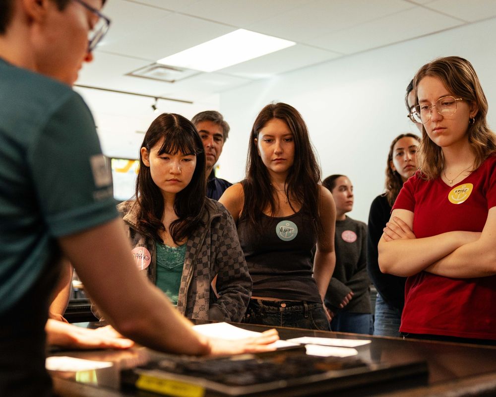 Students from the University of Washington Textual Studies 402: Book Arts course watch a letterpress printing demonstration at Partners in Print.