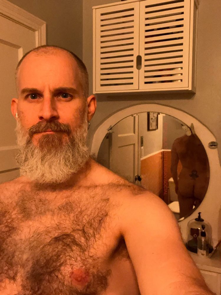 Bearded and hirsute individual taking another selfie in the bathroom, their butt reflected in the mirror behind them.