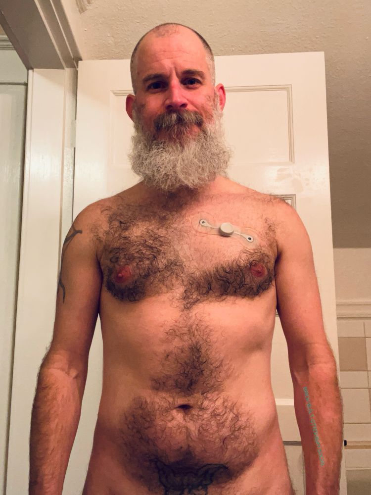 Bearded and slightly less hirsute individual standing in front of an open bathroom door.  A mobile heart monitor is stuck to the shaved down patch on his chest.  It itches like a mutha fucka.  Is it because of hair regrowth or the stickum on the monitor?  Maybe it’s a combination of the two?  We’ll find out in 8 days.  Stay tuned.  
