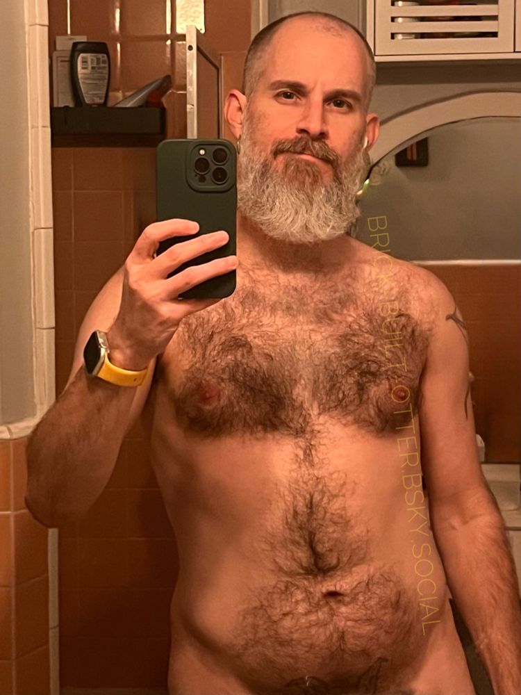 Bearded & Hirsute individual standing in their grey walled and salmon(ish?) tiled bathroom taking a selfie before getting in the shower
