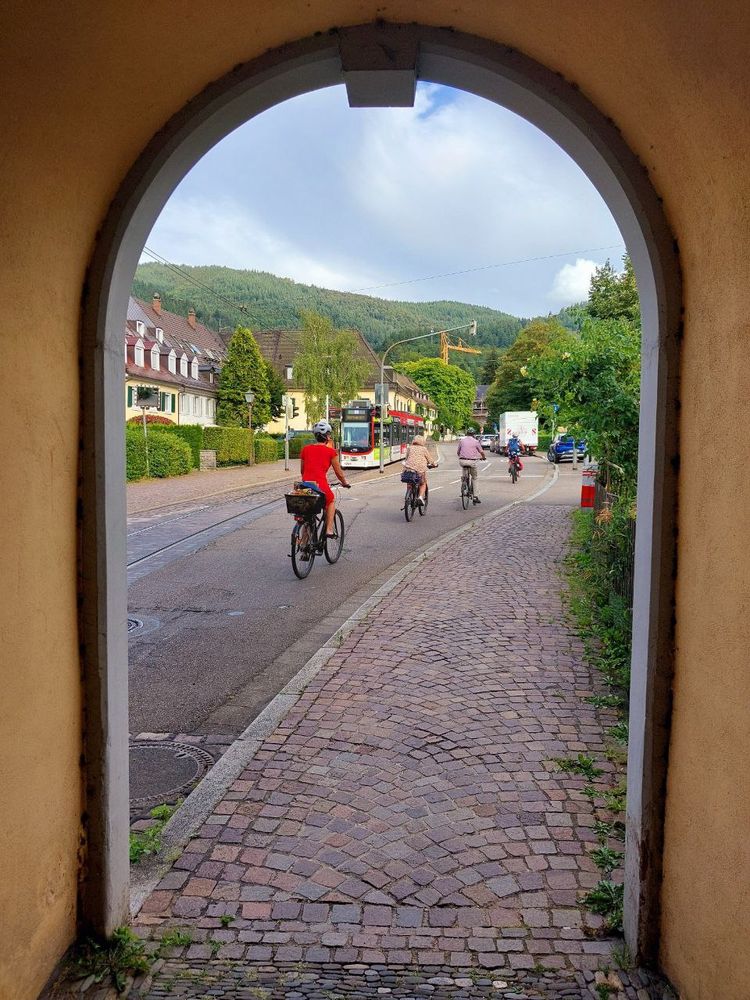 Blick aus einem Torbogen des Torhauses des ehemaligen Günterstaler Klosters auf Radfahrer und die Freiburger Straßenbahn #264 (Linie 2 Richtung Hornusstraße).