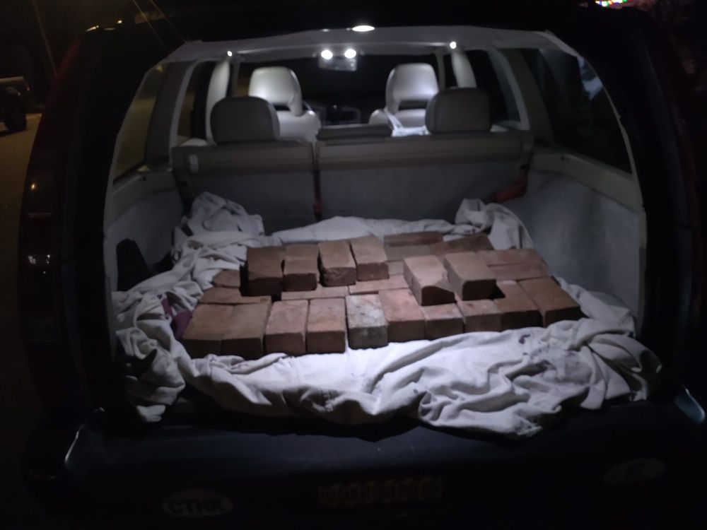 The open trunk of a station wagon at night, with a layer of used bricks resting on a canvas drop cloth. 
