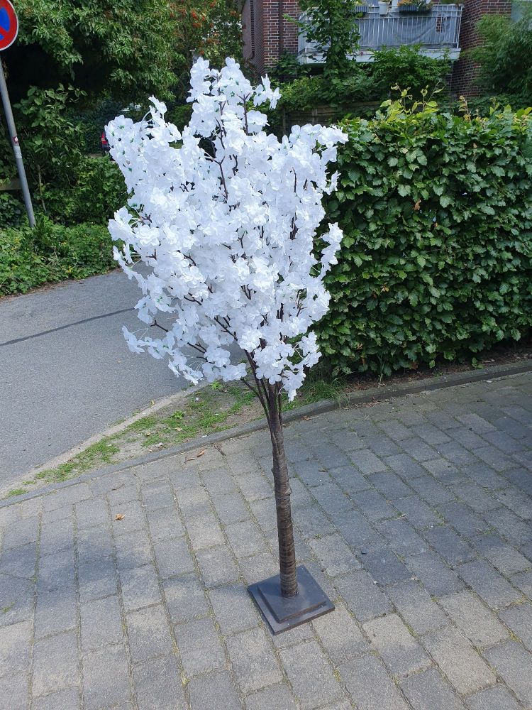 Ein künstlicher Kirschbaum mit weißen Blüten steht auf einem Gehweg.