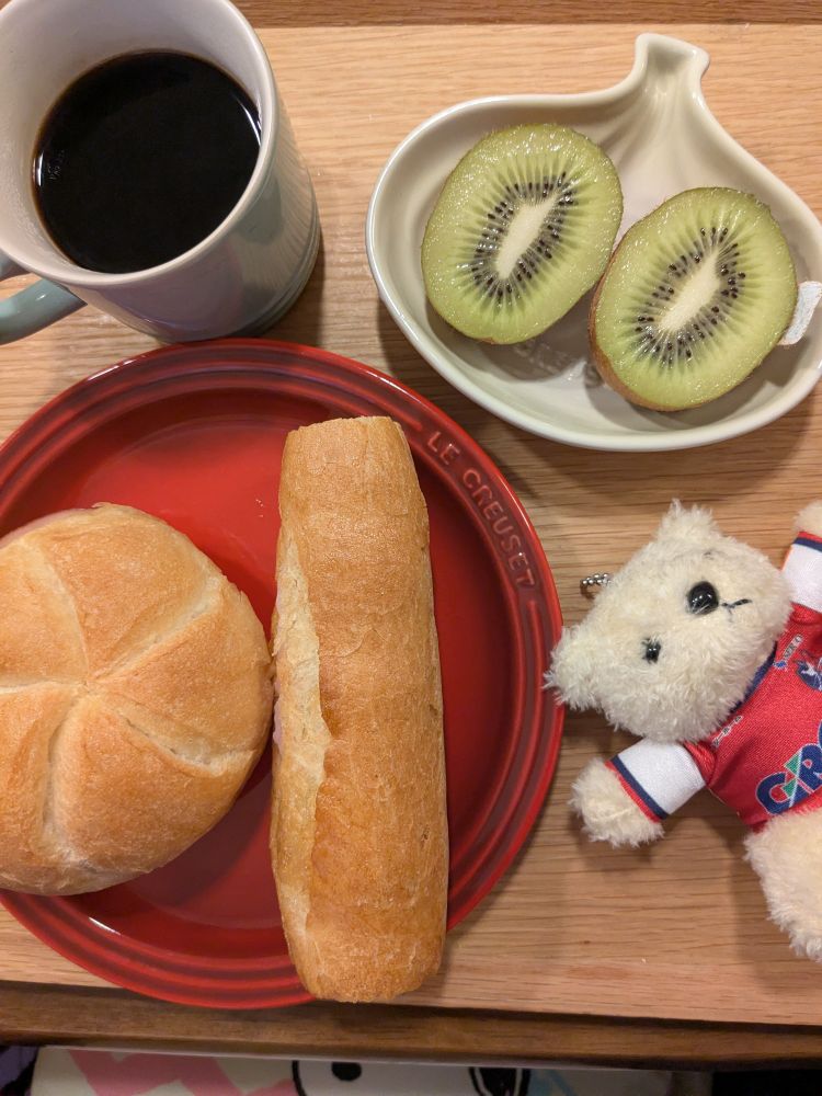 赤い皿にカルネ（丸いフランスパン風にハムと玉ねぎ）とカスクートミニ（細いフランスパン風にハムとチーズ）。玉ねぎ皿にキウイ。水色マグにコーヒー。ファジアーノ岡山ユニくま（かわいい）。