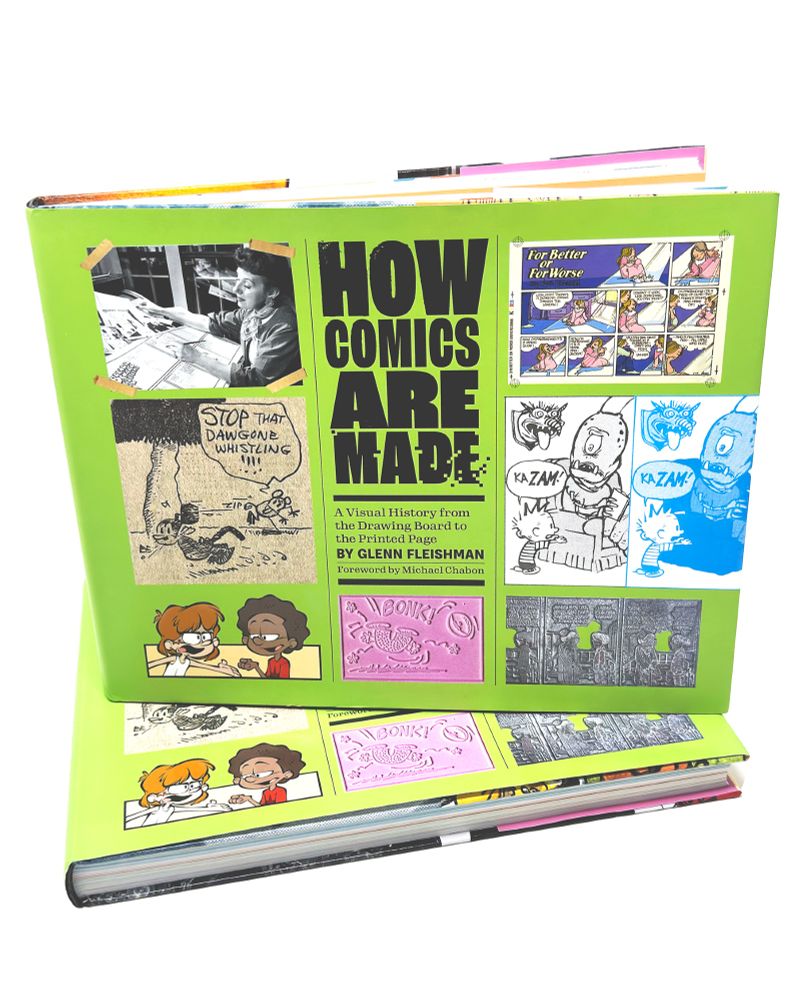 Stack of How Comics Are Made book: green cover with title surrounded by cartoonist, panels, and artifacts. One book upright, slightly open, on top of a another book flat on a table. White background.