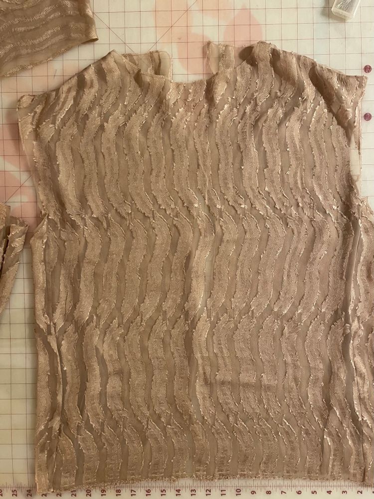 Bodice of a high necked blouse shown flat on a cutting table. It is made of bronze/gold silk chiffon that has been appliquéd in a regular pattern of matched gold vertical squiggles. The effect is almost like animal print. 