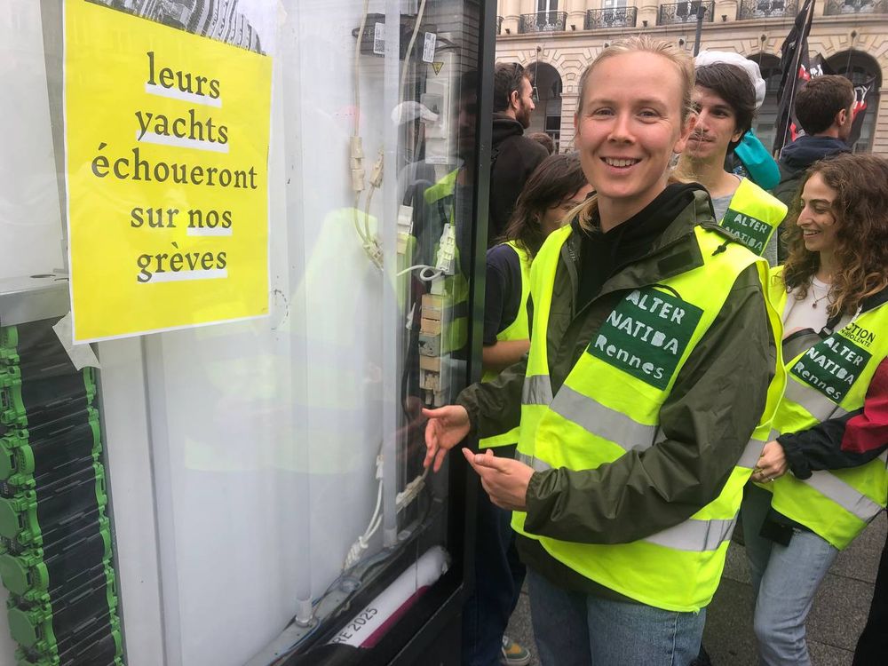 Une personne sourit devant un panneau de pub qui a été vidé. Un nouveau message est placé sur une affiche "leurs yachts échoueront sur nos grèves" 