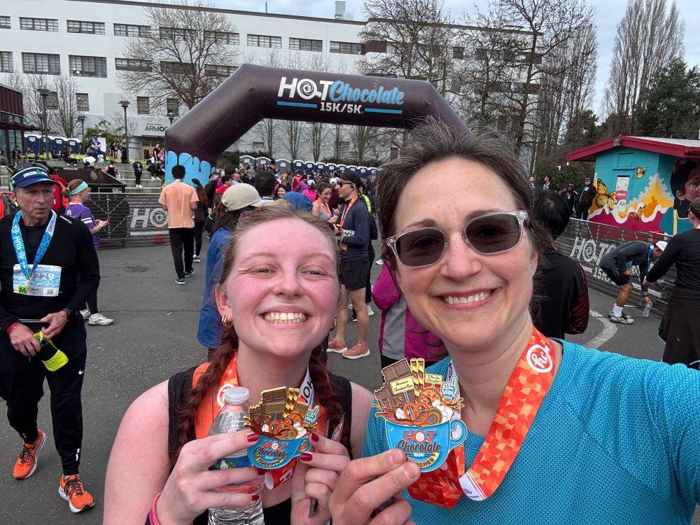 Two females holding finished metals in front to balloon arch stating Hot Chocolate 15k/5k