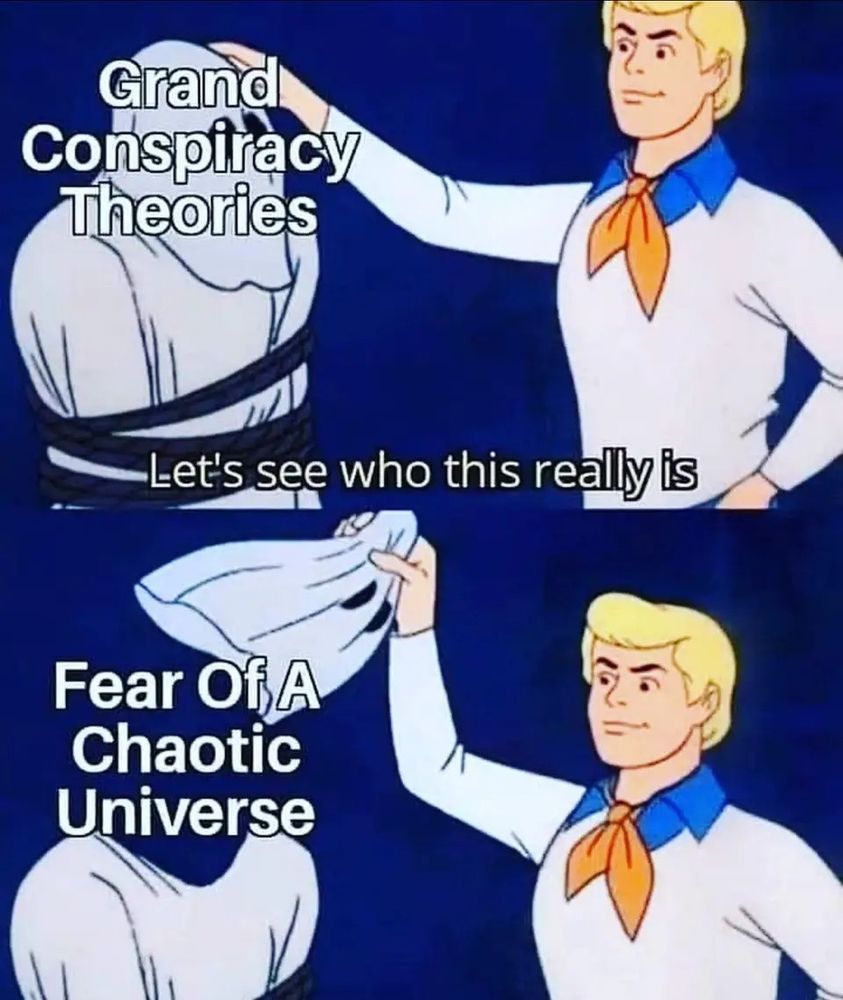 A two-panel Scooby-Doo meme showing Fred pulling off a mask. In the first panel, he's unmasking someone labeled "Grand Conspiracy Theories" with the caption "Let's see who this really is." In the second panel, the mask is removed to reveal "Fear Of A Chaotic Universe" underneath.