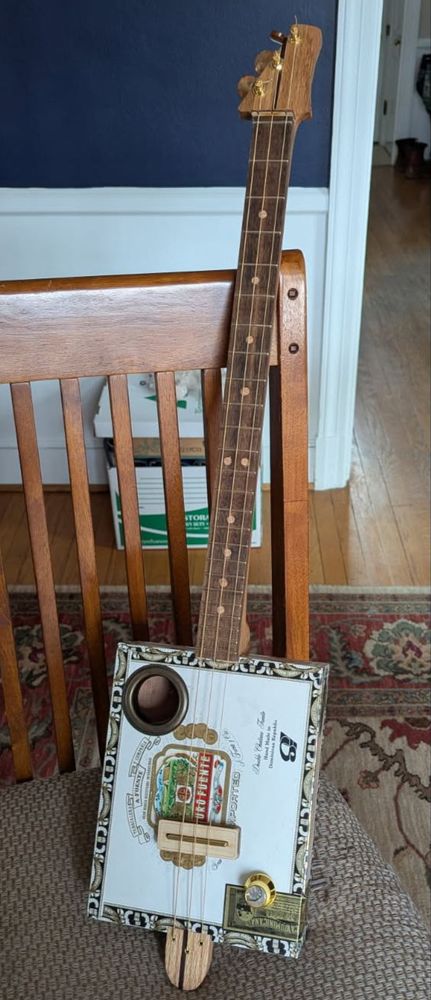 Newly-finished cigar box guitar sitting on a dining room chair