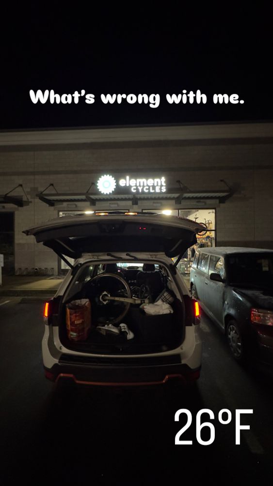 Car with open trunk in front of a bicycle shop. There is a bike in the back. Text with the temperature of 26°F is displayed and also a caption ‘What’s wrong with me’