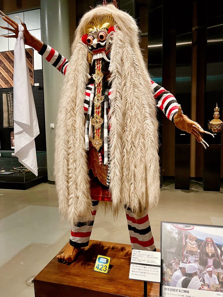 ランダ
制作者:イ・ワヤン・タング 
民族: バリ
国名: インドネシア
年代：2013年製造

災いをもたらす魔女。その力をおそれるバリ島の人びとは、ランダに供物をささげ、劇を演じることでその力をしずめようとする。
とパネルに書かれている。

大きな眼玉が飛び出し、上向きにはえる2本の牙は、象牙のように反り返り、口からたらした長い舌は腹部まである。白い髪もいまにも地面につかんばかりに長い。爪もとても長い。