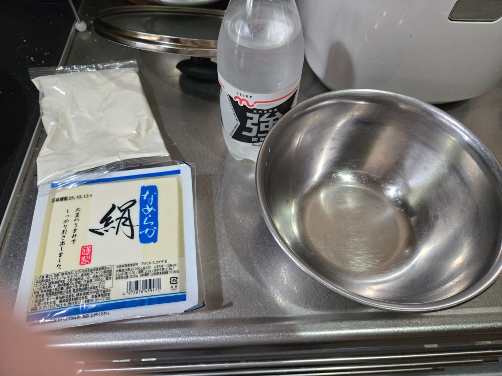 キッチンにて、ホットケーキ粉、豆腐パック、炭酸水、ボウルが置いてある。