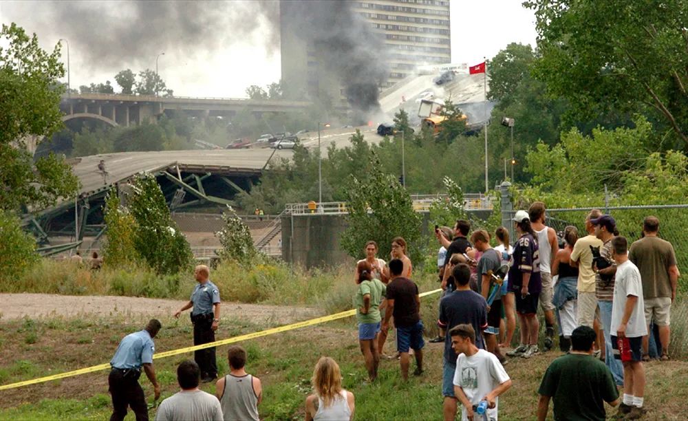 Onlookers view a collapsed bridge behind yellow police tape. 