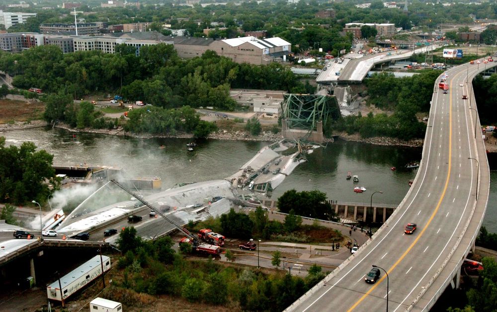 A collapsed bridge span lies in a river as emergency crews work nearby. 