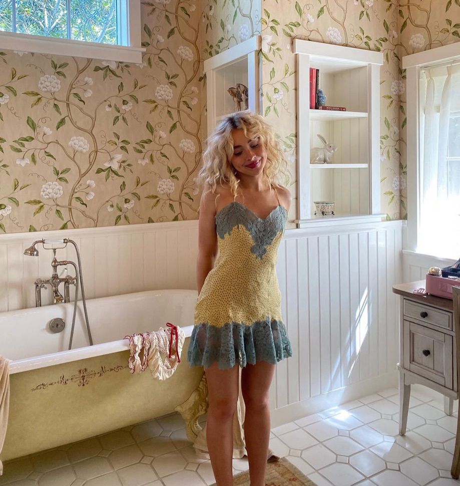 sabrina carpenter being cute in a yellow and white bathroom in a yellow and blue dress