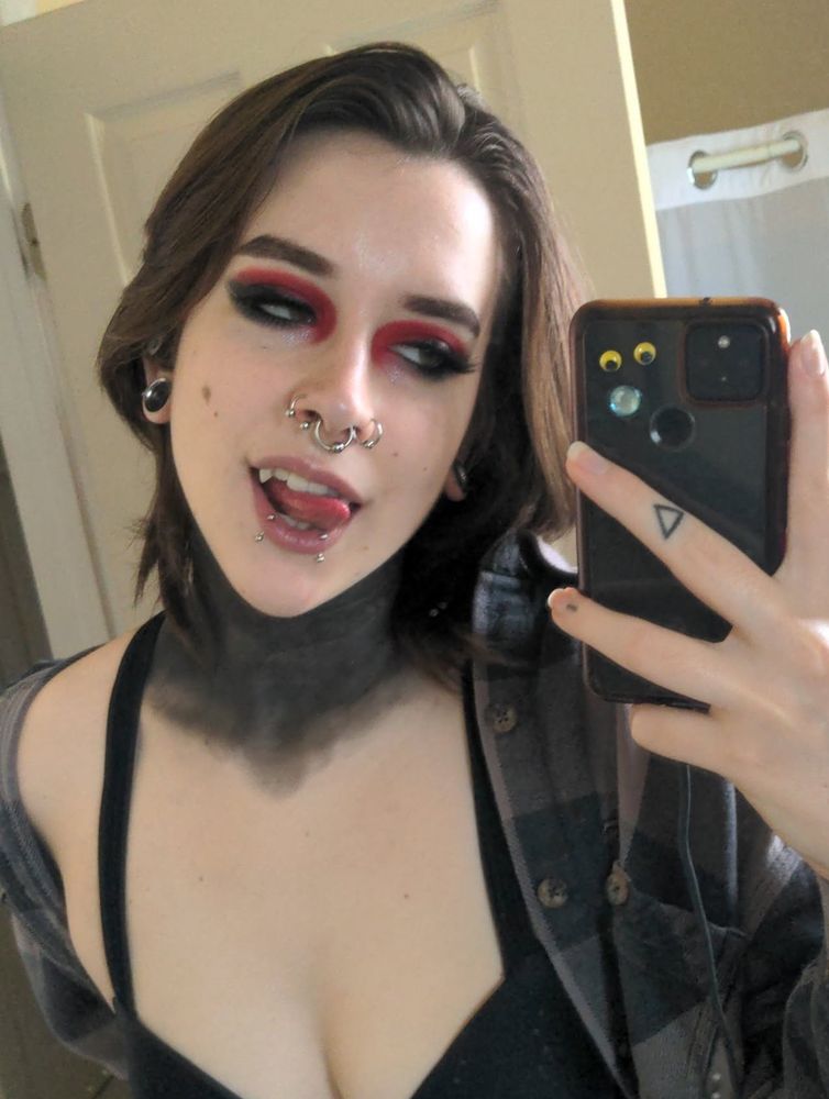 emo girl with 21 pilots neck and red eyeshadow licks her spirit halloween fangs seductively