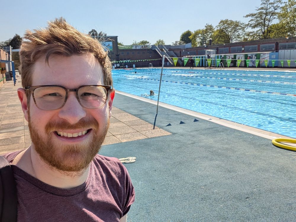 Man standing in front of an open air swimming pool on a sunny day