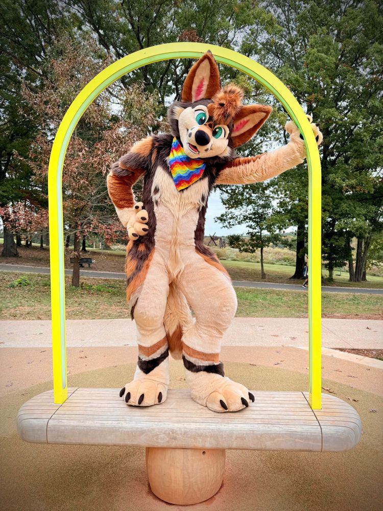 A coyote fursuiter stands on a piece of installation art that prominently features a golden arch