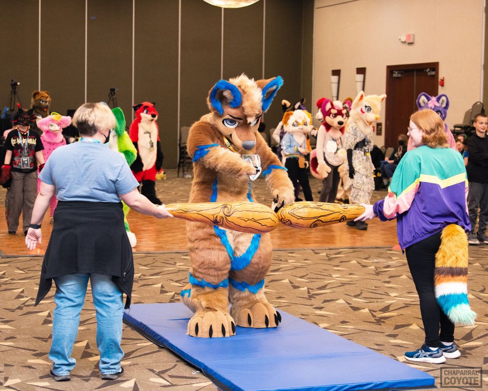 A fursuiter points confrontationally at a limbo bar as though to challenge it 