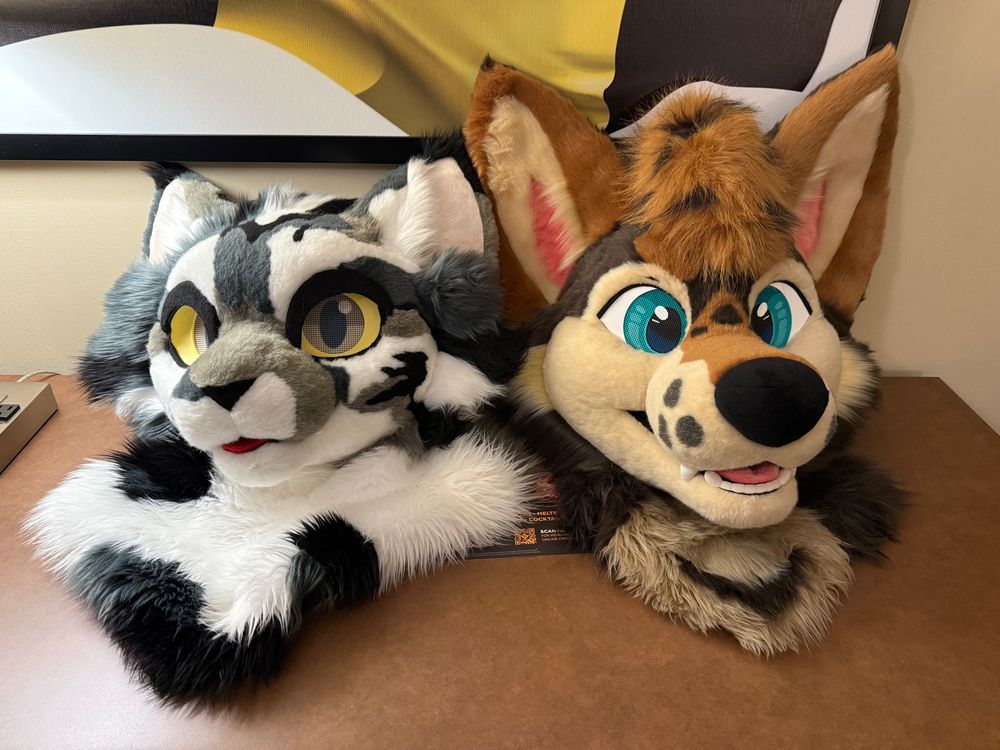 two fursuit heads sitting together on a table 
