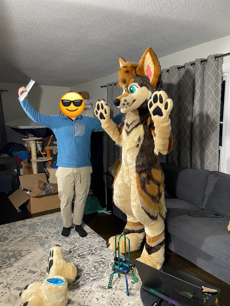 A human being in full suit for the first time holds up his paws for the camera with a helper mimicking the pose nearby