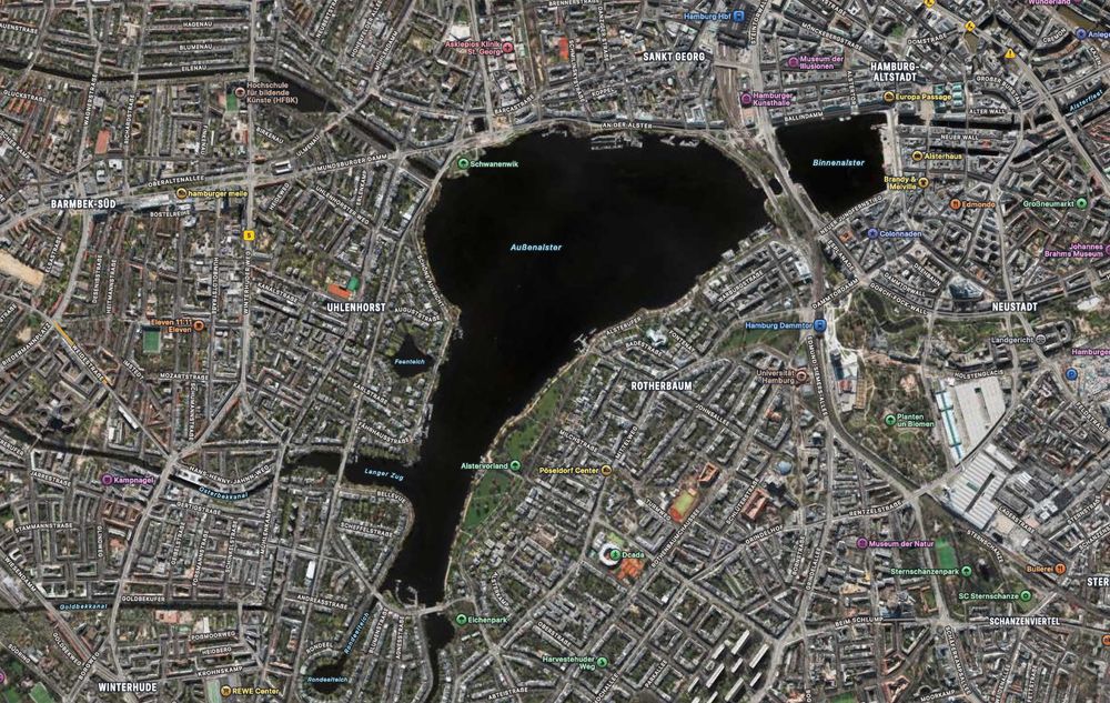 Luftbild der Innenstadt von Hamburg. In der Mitte liegen als dunkler Fleck die Außenalster und die Binnenalster, die sehr entfernt an einen Föhn erinnern.
