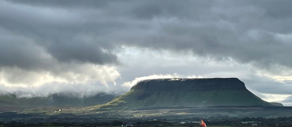 Gray clouds with a patch of sunlight on the lower slope of Benblubin, a flat top mountain