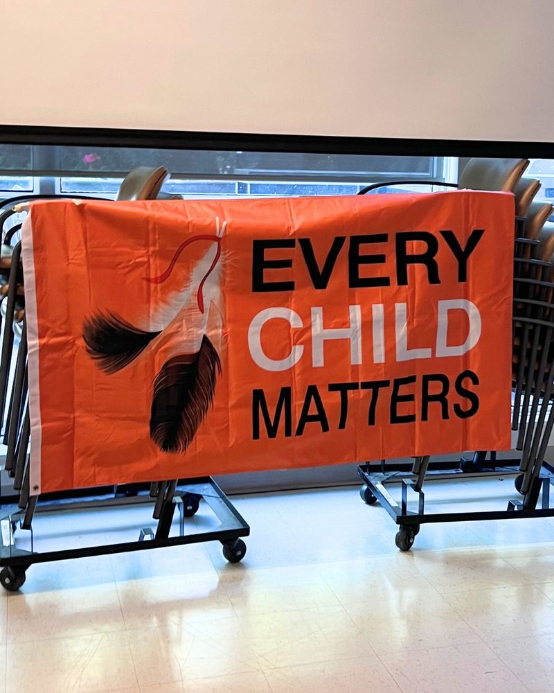 An orange flag with paintings of a pair of feathers and the words EVERY CHILD MATTERS