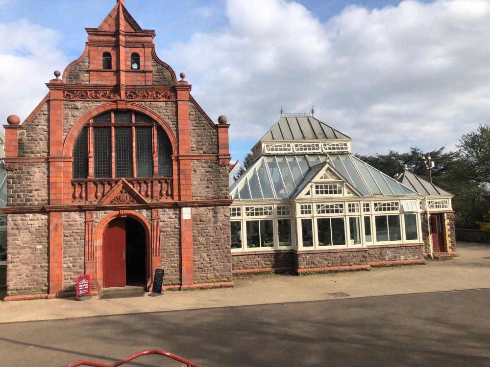 Beautiful tea rooms in a red and brown brick building with a fancy glass conservatory on the right. 