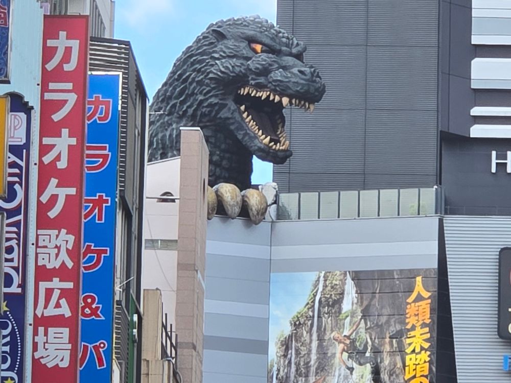A giant Godzilla head statue peering over a building.