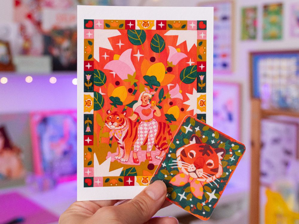 A picture of a hand holding tiger themed printed goodies : a mini print and sticker