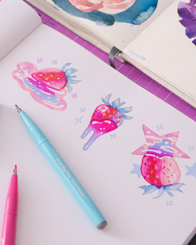 a photo of a sketchbook page featuring colorful and shiny strawberry drawings
