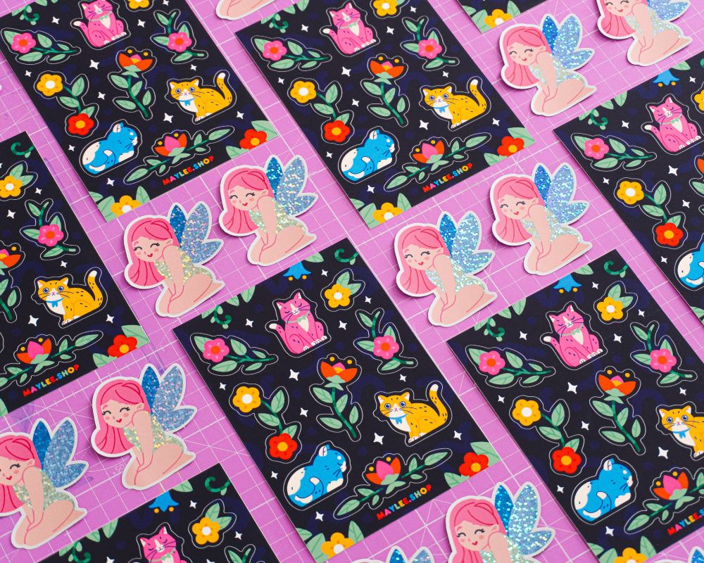a glitter fairy sticker and a cat and flower themed sticker sheet layed flat on a purple cutting mat 