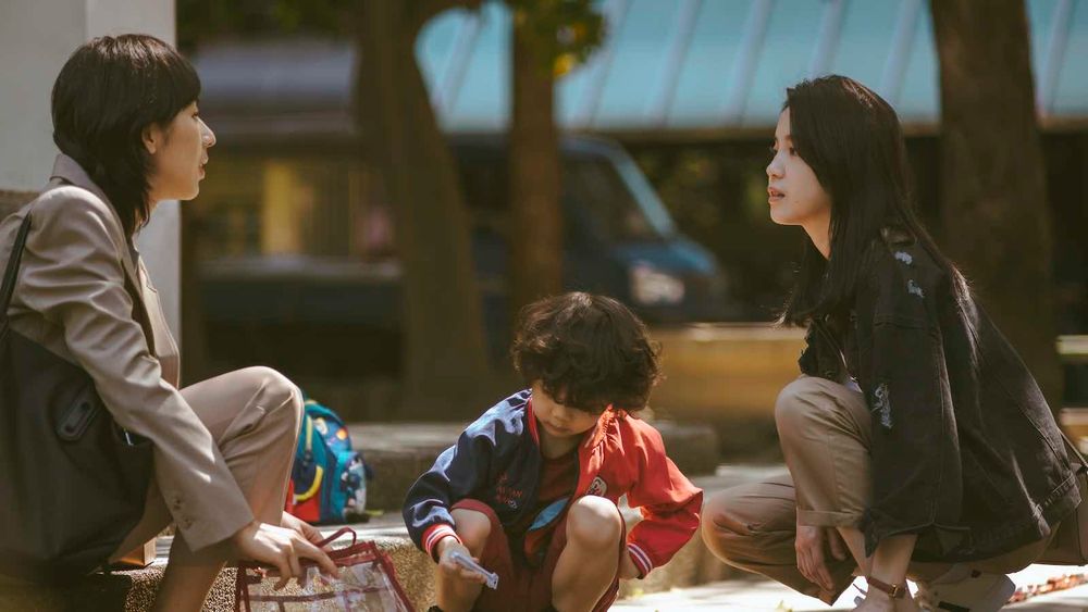 The two main characters of Fragrance of the First Flower, Yi Ming and Ting-Ting, sit at a playground with Yi Ming's child between them.