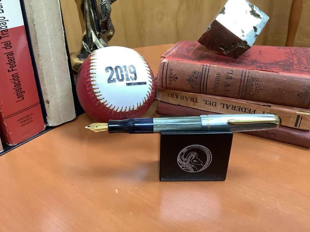 The same pen, uncapped with a black plastic section and a golden steel medium nib. The body has a large ink window, now filled with a mix of J Herbin Perle Boir and Gris Nuage. It posts safely, without risk of turning the piston.