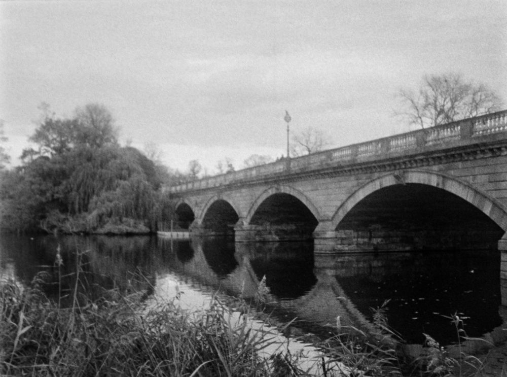 stone bridge with arches across the serpentine lake in hyde park, london