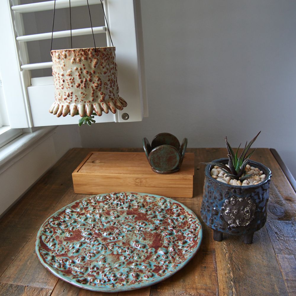 Newly listed product on Etsy. Beige and brown upside down sculptural planter with succulent, dark brown and green tea light candle holder made out of five circles, dark brown a blue planter with cacti, round platter with bumpy texture in brick brown and turquoise glaze.