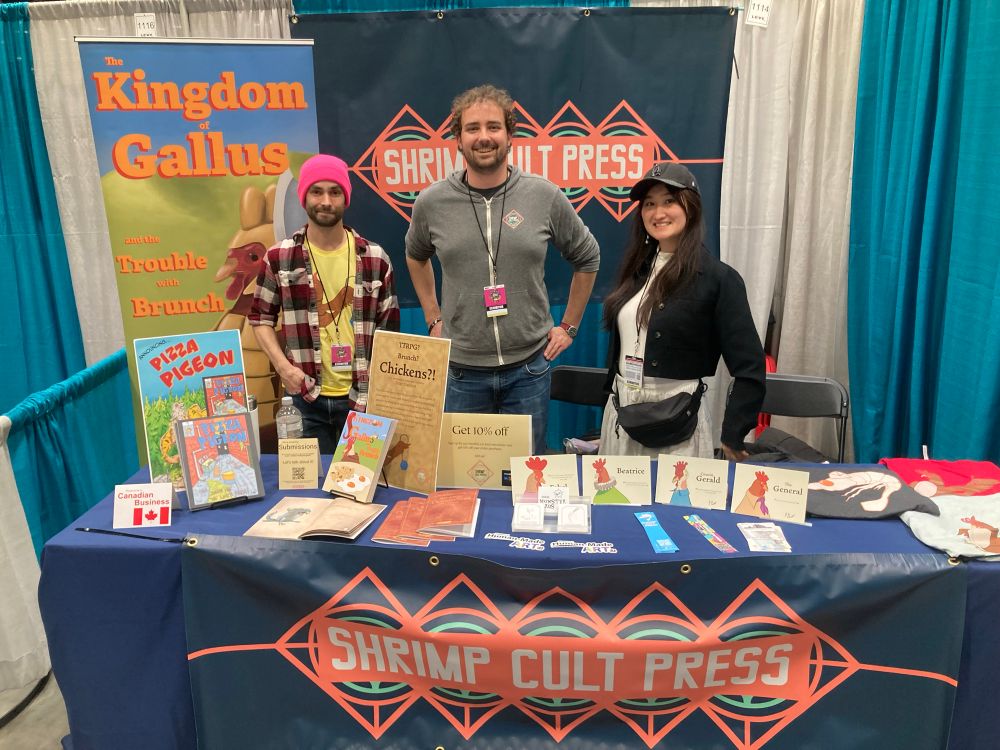 Three cool folks standing at a convention table for Shrimp Cult Press. 