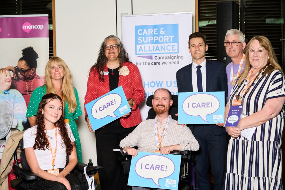 Photo of a group of people holding signs that say 'I care!' There is an MP,  two working age adults in wheelchairs, and several unpaid carers.