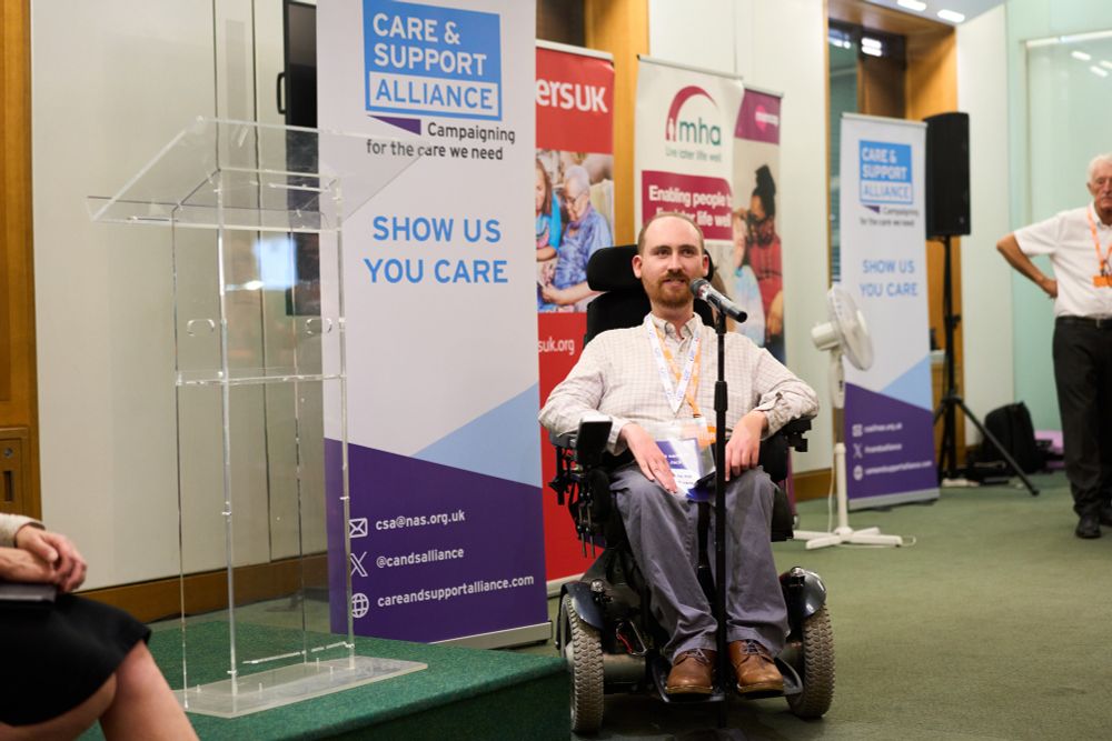 Photo of Jack, who uses an electric wheelchair, speaking into a microphone.