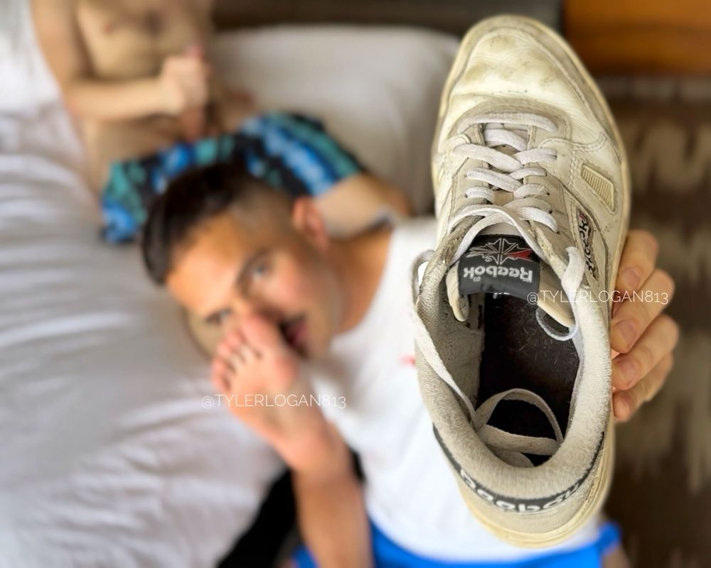 Tyler holding a worn Reebok sneakers into the camera, while sniffing Jake’s foot (whom the shoe belongs to), while he’s lying back on the bed stroking his cock.